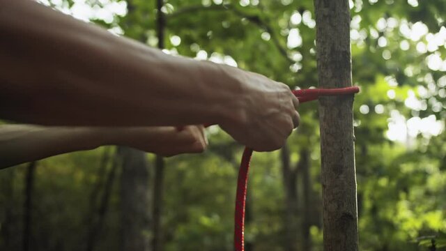 The survivalist ties the rope to the tree, close-up. 