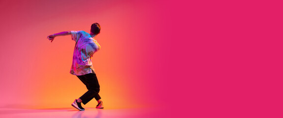 Back view of young stylish man dancing hip-hop isolated over colorful gradient background in neon light. Flyer