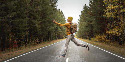 Traveler with a backpack on a road along the forest is jumping with his arms outstretched. Concept...