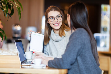 two girls in a cafe with a tablet and laptop.