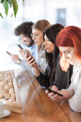 Four friends sitting at a cafe bar looking at phones.