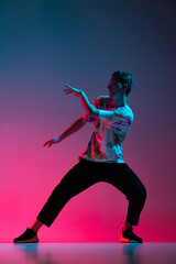 Vertical portrait of young man dancing hip-hop isolated over gradient pink purple background in neon light
