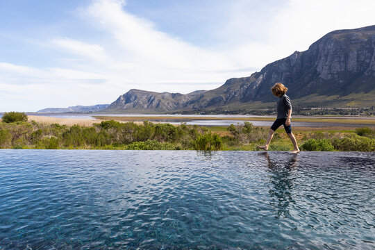 Eight year old boy walking around the edge of an infinity pool, a mountain backdrop