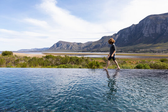 Eight year old boy walking around the edge of an infinity pool, a mountain backdrop