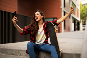 Fototapeta na wymiar Portrait of young beautiful girl with skateboard. Happy smiling woman using the phone