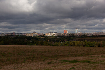 The sky is filled with dark clouds, the fields are empty. A ray of sunlight shines on a red building in the distance.