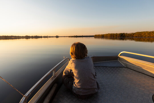Young boy sitting at the stern of a boat on the Okavango Delta at sunset