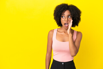 Fototapeta na wymiar Young African American woman isolated on yellow background whispering something with surprise gesture while looking to the side