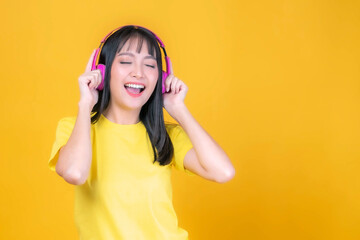 beautiful Asian young woman cute girl with bangs hair style in yellow shirt smiling with pink headphone listen to her favorite song isolated on yellow background , copy space