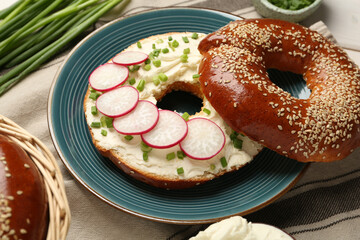 Delicious bagel with cream cheese, green onion and radish on table, closeup