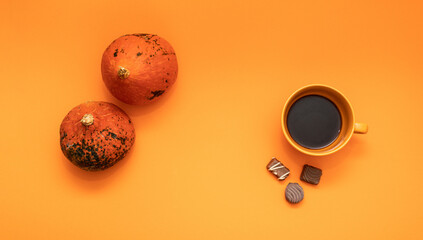 Modern autumn pumpkin concept with the remains of chocolate and fresh made cup of coffee on an orange background. Minimal flat lay idea for October Halloween and trick or treat season.
