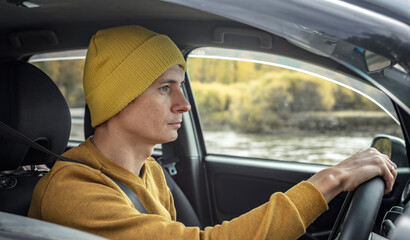 Man is driving a car along the river and the beautiful autumn forest. Concept of nature, travel and...