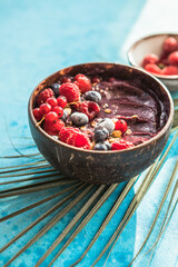 Frozen acai smoothie in coconut shell with raspberries, banana, blueberries,  fruit and granola on concrete background. Breakfast, healthy meal for summer vibes, top view, space for text
