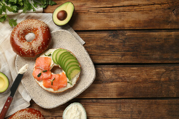 Delicious bagel with cream cheese, salmon and avocado on wooden table, flat lay. Space for text