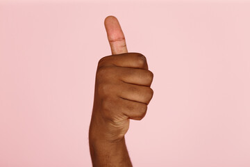 Young African-American man hand shows thumb-up gesture to cheer up on light pink background in studio extreme close view