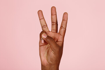 Young African-American man hand shows three fingers gesture on light pink background in studio extreme close view
