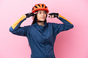 Teenager cyclist girl isolated on pink background having doubts and thinking