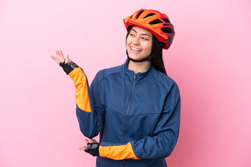 Teenager cyclist girl isolated on pink background extending hands to the side for inviting to come