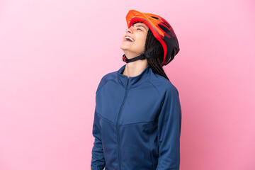 Teenager cyclist girl isolated on pink background laughing in lateral position