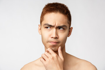 Beauty, skincare and men health concept. Headshot of serious naked asian man thinking, touch chin...