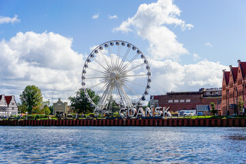 ferris wheel and historic buildings with city sign on the Motlawa River in the Old Town of Danzing