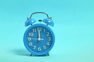 Blue alarm clock on blue background it shows twelve clock, night and lunch time.