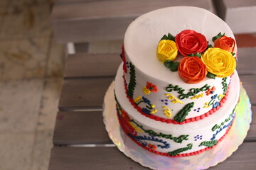 Two-tiered white wedding cake decorated with pink flowers on a white wooden background.