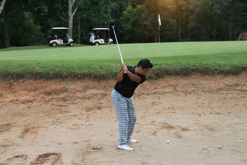 Golfer hitting golf ball on bunker of sand in course.