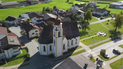 Great circling footage of a drone in the alps flying around a beautiful church with traditional houses in the village in the back in Europe
