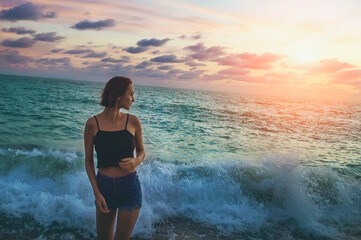 A girl stands at sunset against the background of the sea surf. Vacation, travel concept.