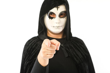 Person with in white mask with cross on forehead and black velvet cape with unfocused hood, pointing at camera with focused hand, on white background. Carnival, Halloween and Day of the Dead concept.
