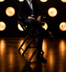 Stylish fashionable unrecognizable man sits on a chair in a jacket in a white shirt in a dark room...