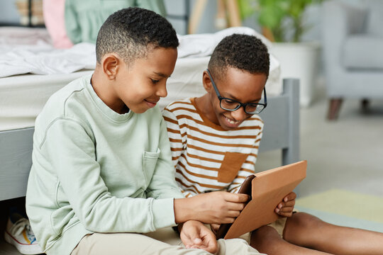 Portrait of two teenage African-American boys using digital tablet together in cozy room, copy space