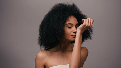 young african american woman enjoying odor of perfume isolated on grey