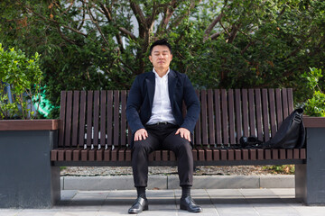 Obraz premium Asian businessman tired after work, sitting on a bench with fatigue and headache, has stress and panic attacks