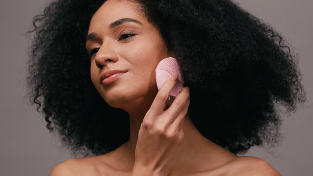 brunette african american woman using silicone cleansing gadget isolated on grey