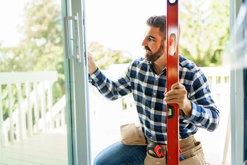 handsome young man installing bay window in a new house construction site with level