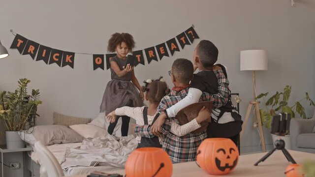 Slowmo shot of African-American kids in Halloween costumes making spooky videos on smartphone while celebrating Halloween together at home