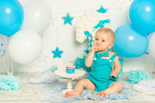 baby eats birthday cake and celebrates first birthday in photo zone in blue color with balloons and cake