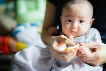 Asian Baby getting finger nails cut  by his mother with scissors the concept of motherhood and care. 