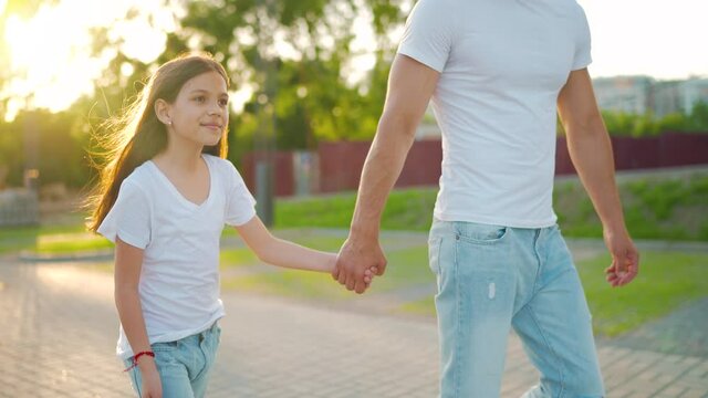 Dad and daughter walk around their area at sunset. Child holds father's hand. Slow motion