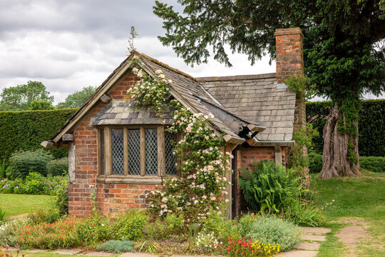 Very old small red brick garden house with slate roof, mullioned windows and pink climbing rose.
