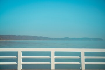 Obraz premium Sea view in the morning through the wooden pier. Foggy weather at the seaside during a summer morning with white painted handrail