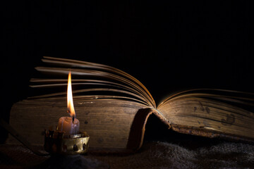A candle burns next to an open old book. the concept of secret knowledge and mysticism. Selective focus on a candle flame.
