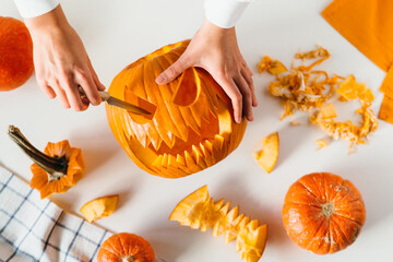 Happy halloween, decoration and holidays concept. Young woman hands with knife carving pumpkin or...