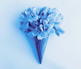 Blue ice cream cone with blue peony in the center of the gray background. Close-up. Flowers concept.
