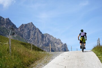 Man on a bicycle on a hilltop in rear view. There are Alp mountains on the left hand side. Cycling...