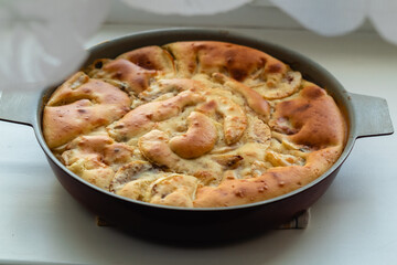 Traditional round golden apple pie on a light table on a blurry foreground.