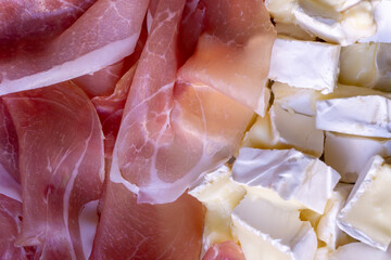 Thin slices of jamon and brie cheese pieces close up food background