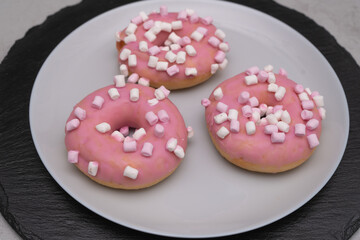 Donuts in sweet glaze on a light plate and a black slate tray